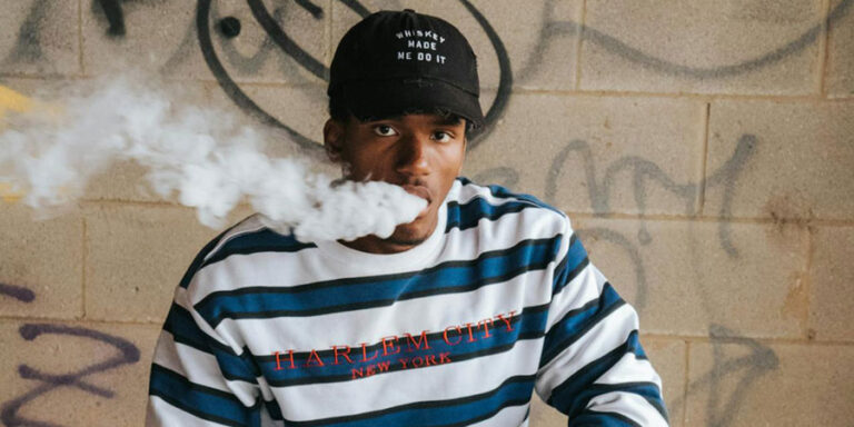 a black man wearing a black cap, blue and white striped sweater while vaping